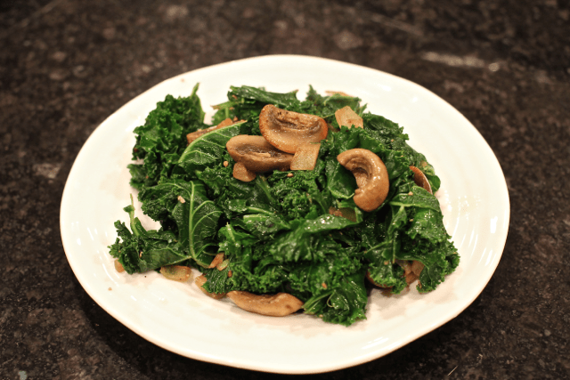 A small white plate piled with a mixture of sautéed mushrooms and kale.