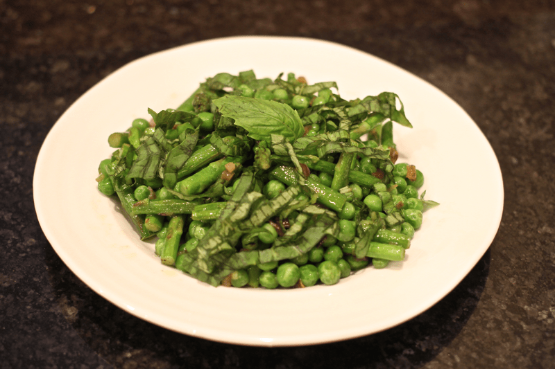 A low white bowl full of a mixture of asparagus and peas with fresh basil