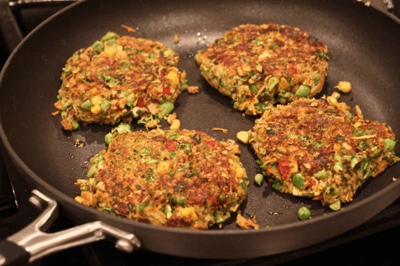 Homemade healthy veggie burgers being cooked in a skillet.