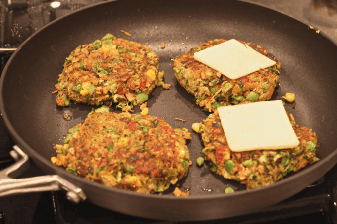 Veggie burgers cooking in a skillet with cheese on top of two of them.