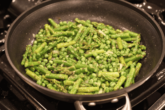 A large skillet with a mixture of shallots, green peas and cut asparagus spears all cooked together.