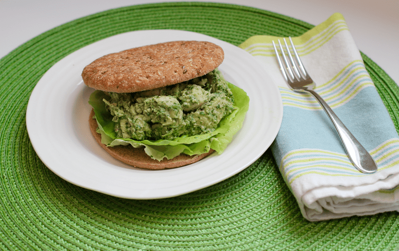 A pesto chicken salad sandwich on a white plate set on a green placemat.