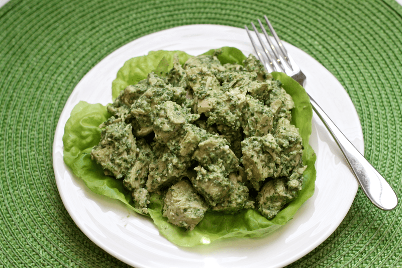 Pesto chicken salad served on lettuce leaves on a white plate with a fork to the side.