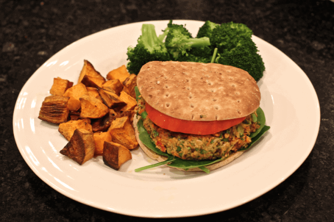 A veggie burger sandwich served with sweet potatoes and broccoli.