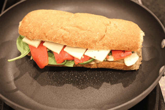 A panini sandwich in a skillet as it\'s being cooked.