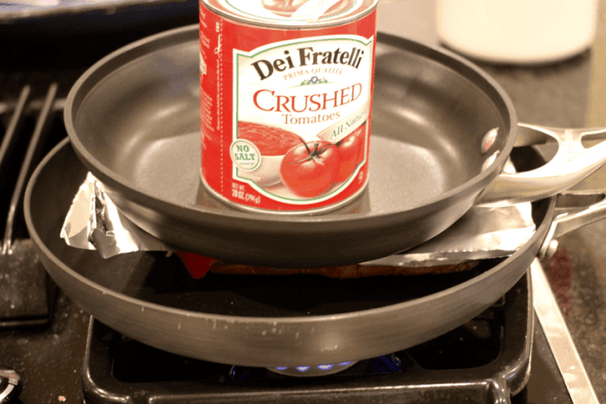 A small skillet with a heavy can of crushed tomatoes on it to weigh down a pressed panini in the larger skillet underneath.