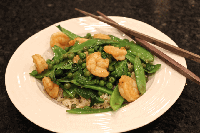 Shrimp and snow pea stir fry served in a low white bowl with wood chopsticks to the side.