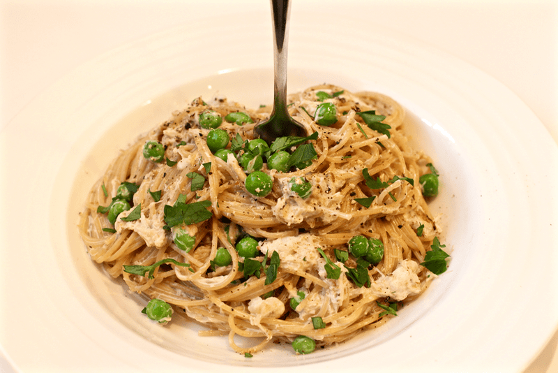 Creamy pasta with crab and peas in a bowl with a fork stuck in it.