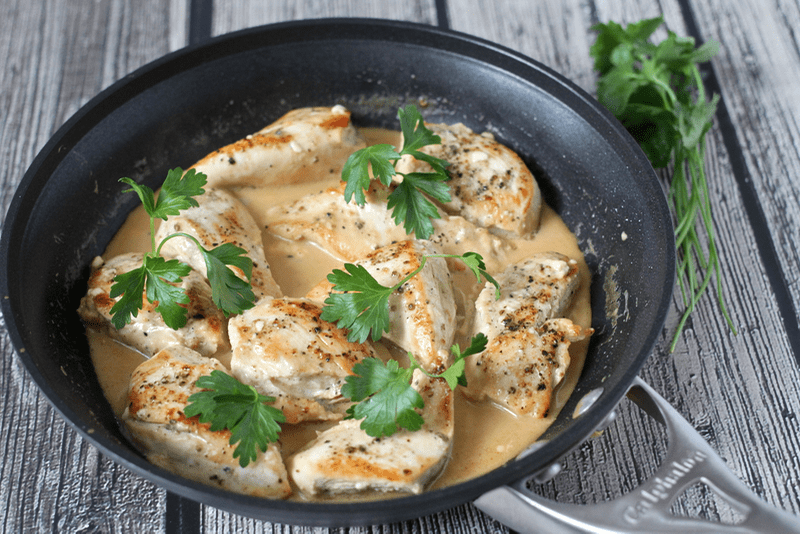 Chunks of chicken breasts cooked in a pan with a creamy sauce and topped with fresh parsley