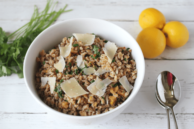 Farro pilaf served in a white bowl with lemons and parsley nearby
