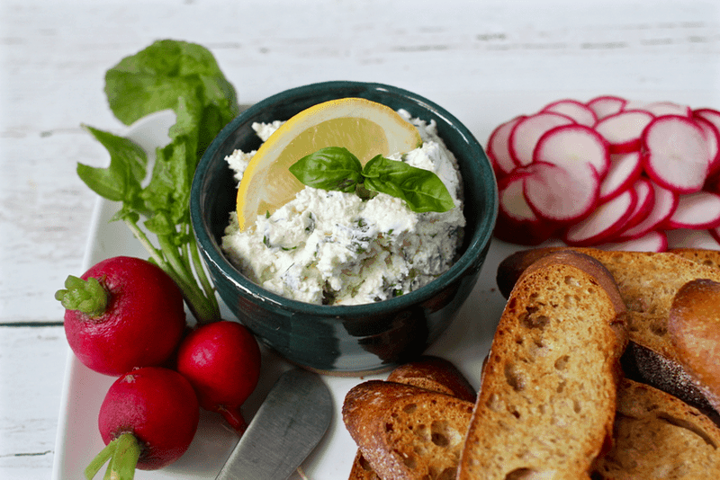 Cheese and herb spread served in a small green dish with baguette slices