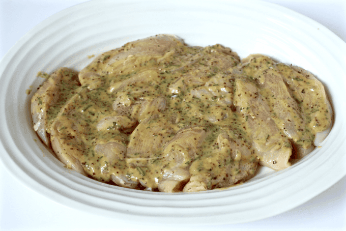 Sliced chicken pieces in a large casserole dish with a honey mustard mixture on top before being cooked.