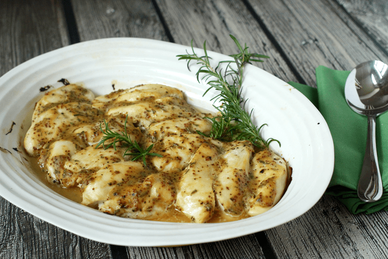 Baked honey Dijon chicken with rosemary for garnish in a large white baking dish.