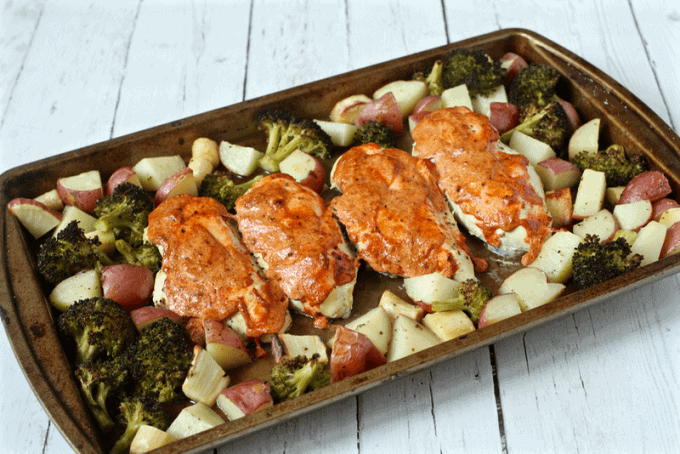 A sheet pan with four roasted chicken breasts with a creamy seasoning on top surrounded by roasted diced potatoes and broccoli florets.