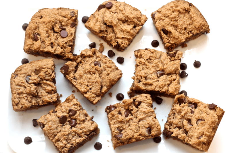 Peanut butter chocolate chip bars cut in squares and scattered on a counter with chocolate chips scattered around.