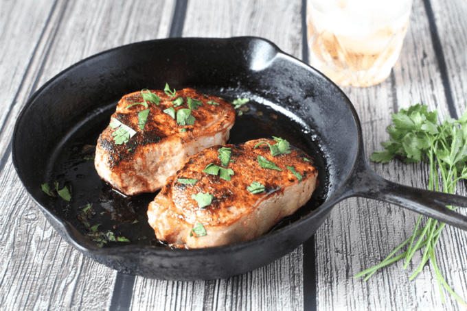 Seared pork chops with a spice rub in a cast-iron pan with parsley sprinkled on top