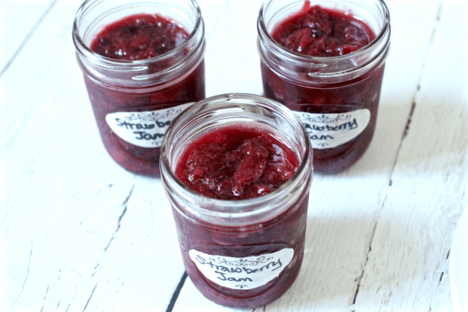 Three small glass jars full of homemade strawberry jam with labels on the front