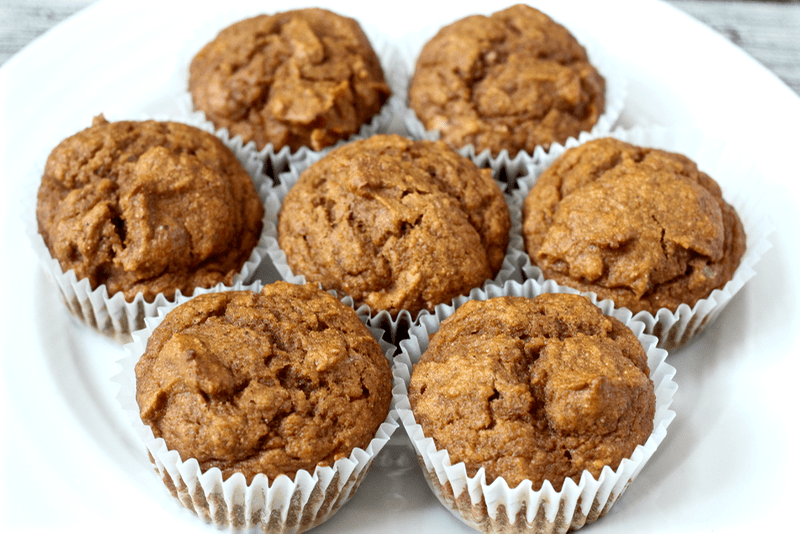 Whole wheat pumpkin muffins in their wrappers and arranged on a white plate.