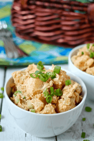 Potato salad served in a small white bowl with green onions on top