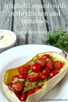 A halved spaghetti squash with shredded pesto chicken and halved cherry tomatoes mixed in and a bowl of Parmesan cheese in the background.