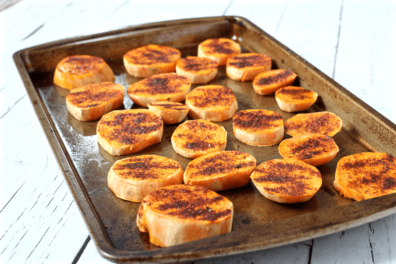 Roasted sweet potato round slices with a spicy seasoning spread out on a baking sheet.