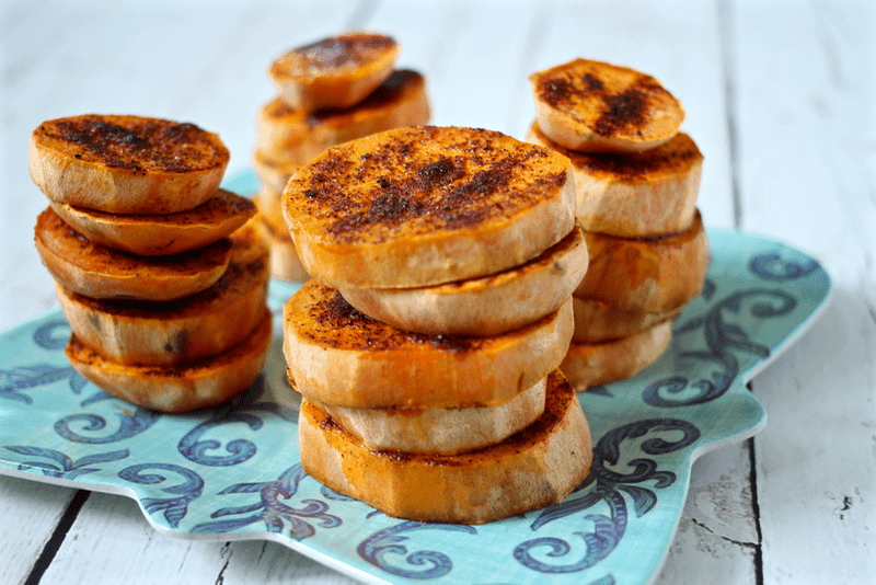 A stack of spiced baked sweet potato rounds on a teal plate.
