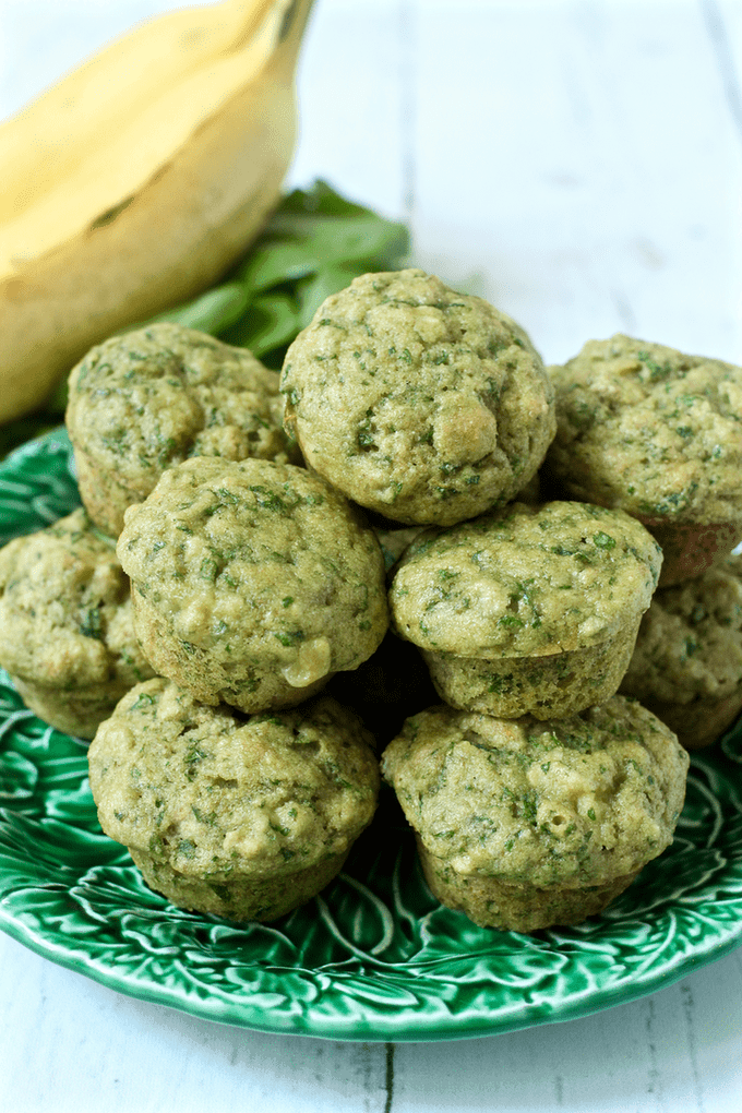 Mini spinach banana muffins stacked all together on a green leafy plate.