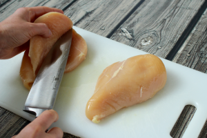 A knife slicing a chicken breast and a hand opening it up