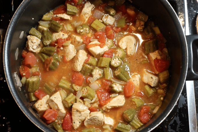 A Cajun chicken stew with okra and tomatoes simmering in a large pot.