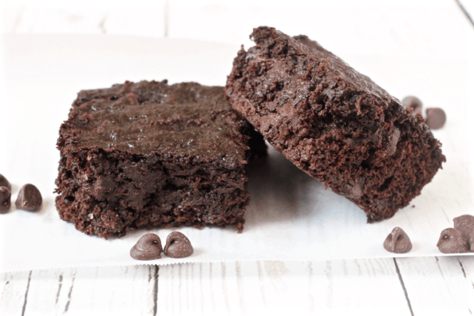 Two chocolate chip zucchini brownies with chocolate chips scattered around them.