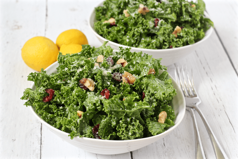 Citrus kale salad with walnuts, dried cranberries and Parmesan cheese served in white bowls
