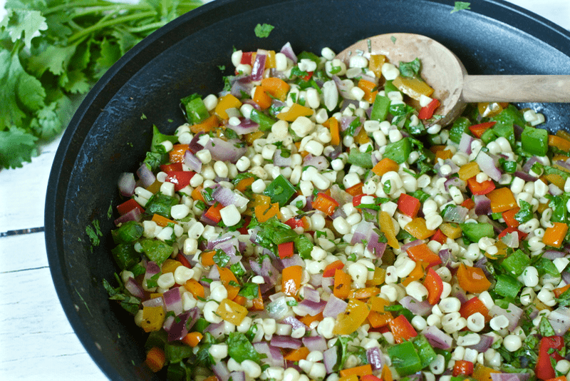 Close up of a corn and pepper saute in a large skillet with a wooden spoon