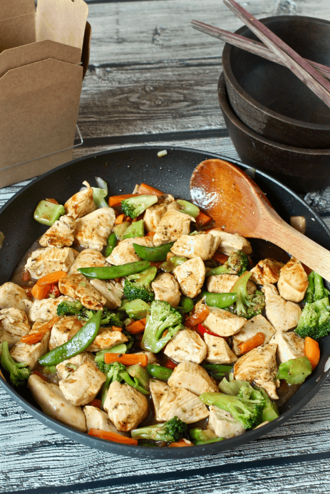 A large skillet with a chicken stir fry mixture made with frozen veggies and a wooden spoon to the side.
