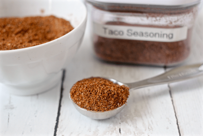 A teaspoon holding a scoop of homemade taco seasoning with a small bowl of it in the background