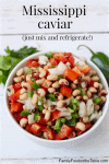 A white bowl with a black eyed pea appetizer dip with peppers and onions and fresh herbs and a jalapeno pepper in the background.