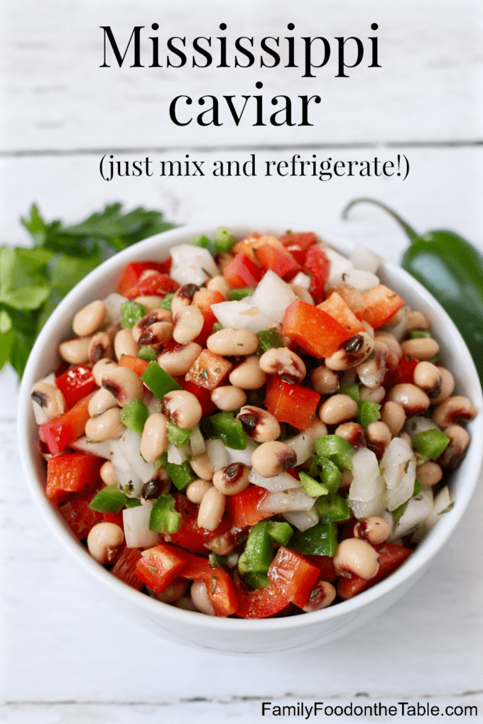A white bowl with a black eyed pea appetizer dip with peppers and onions and fresh herbs and a jalapeno pepper in the background.