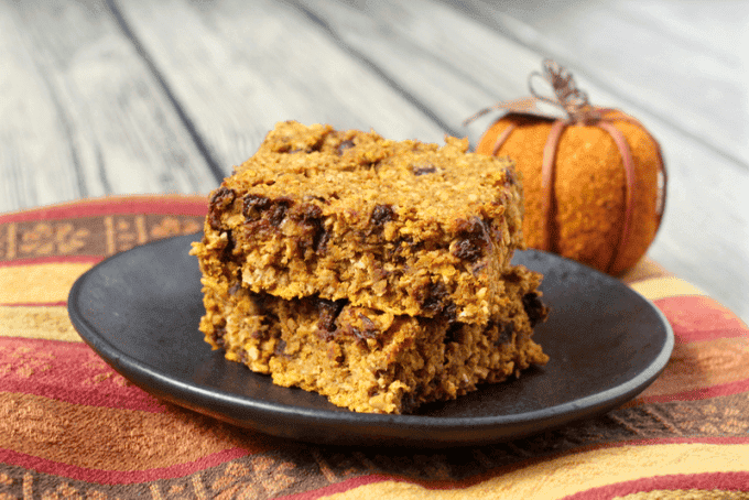 Two squares of pumpkin chocolate chip oat bars stacked on a black plate.