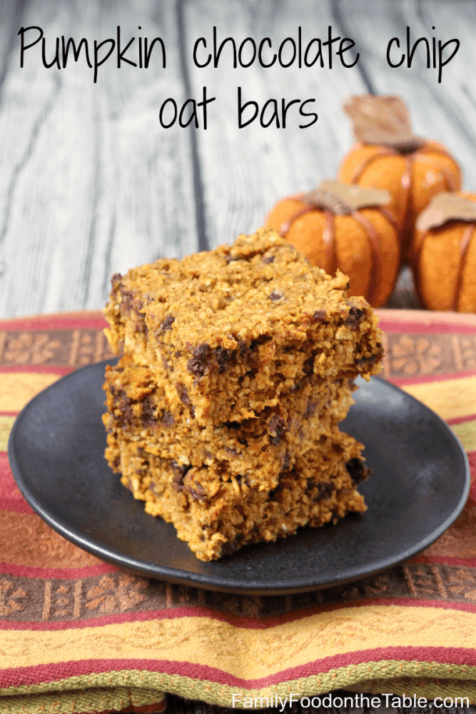 A stack of three square pumpkin chocolate chip oat bars on a black plate with faux mini pumpkins in the background.