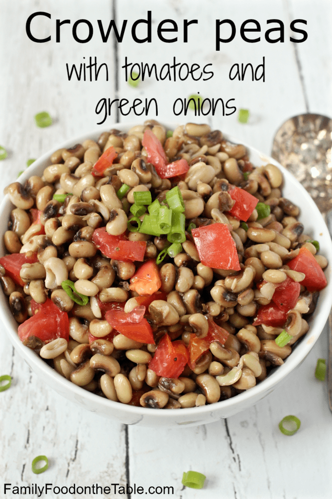 A bowl full of crowder peas with chopped tomatoes and sliced green onions and a spoon to the side.