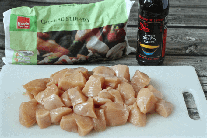 Chopped chicken on a cutting board with frozen veggies and stir fry sauce in background.