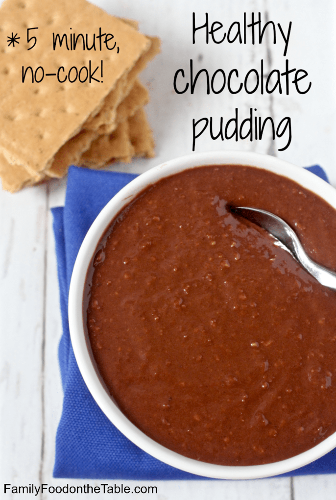 A spoon resting in a white bowl of homemade healthy chocolate pudding with a stack of graham crackers to the side.
