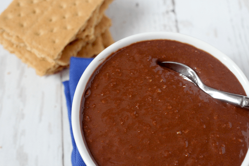 A small spoon resting in a bowl of a homemade chocolate pudding with graham crackers to the side.