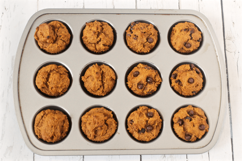 Peanut butter pumpkin muffins, half with chocolate chips, in a muffin tin after baking.