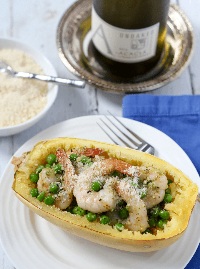 Spaghetti squash with shrimp, peas and pesto is an easy, healthy weeknight dinner that's just 4 ingredients! A white plate with a spaghetti squash half stuffed with green peas and shrimp with pesto.