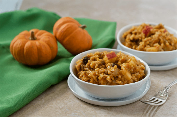 Brown rice salad with apples and pumpkin served in a small white bowl with mini pumpkins in the background