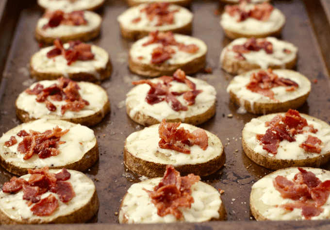 A sheet pan with potato slices topped with melted cheese and cooked, crumbled bacon.