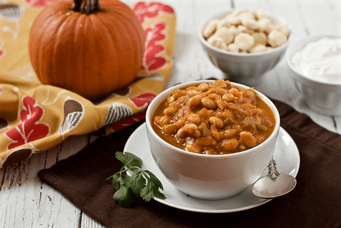 Pumpkin white bean chili served in a small white bowl with toppings in the background