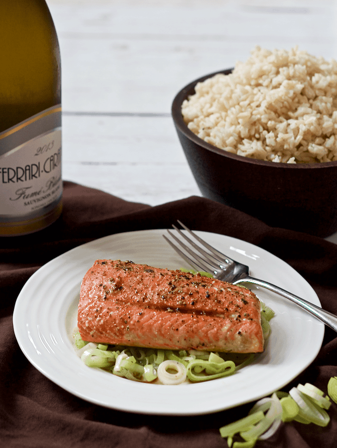 A plate with sautéed leeks topped with a piece of salmon and a bowl of rice in the background