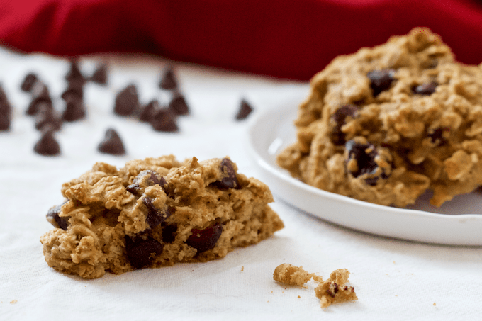 A half of a cookie with chocolate chips and dried cranberries alongside a plate full of the cookies.