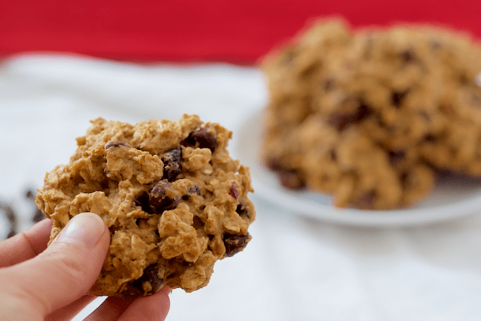 A hand holding up an oatmeal cranberry chocolate chip cookie from a plate of cookies.
